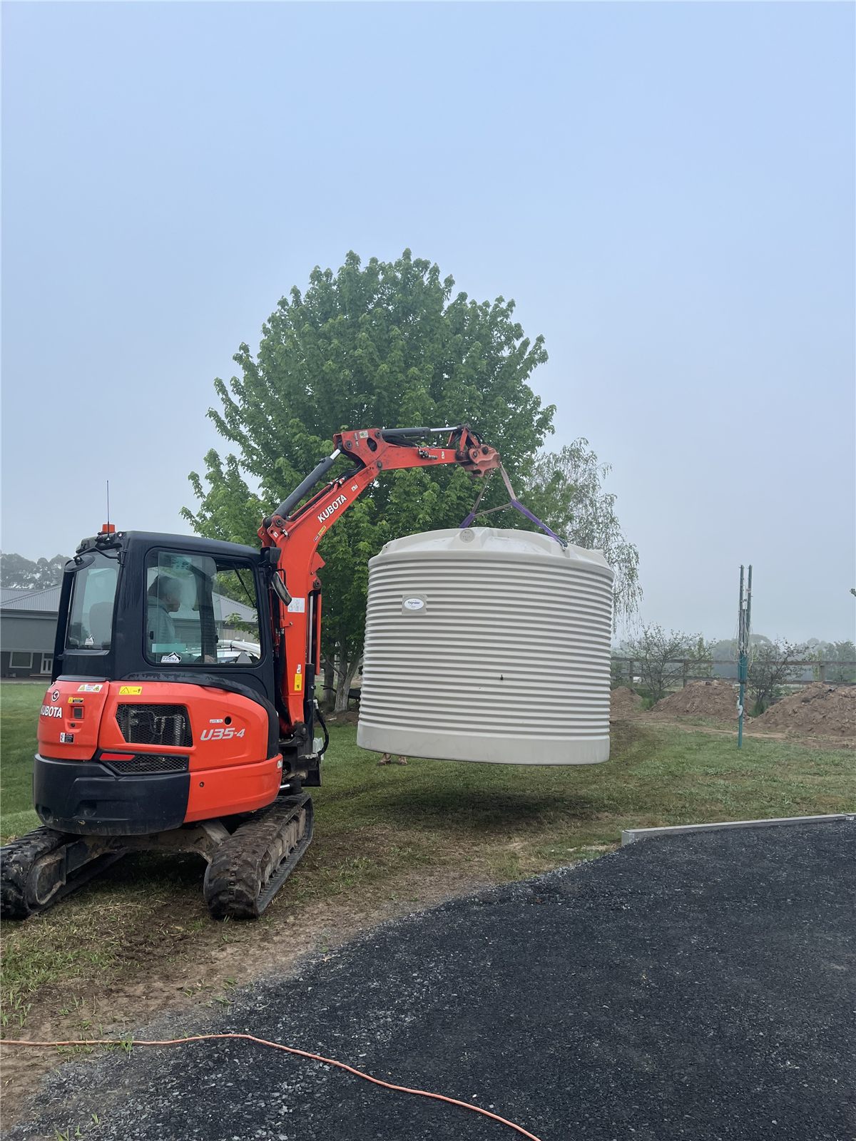 Excavator lifting a rainwater tank into position